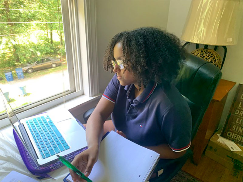A high school student sits at a laptop near a window at home, one of 215 students who connected virtually to NASA's 2020 event.