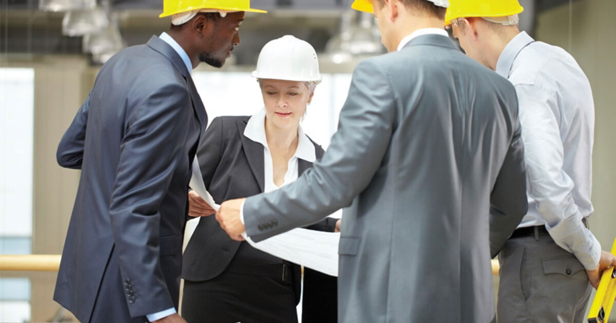 Engineering management staff gather around a large print out in a warehouse setting.