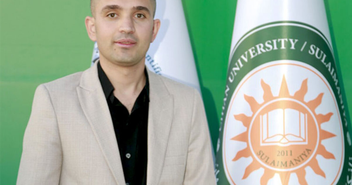 Photo of Sadiq Karim Omer standing next to a flag