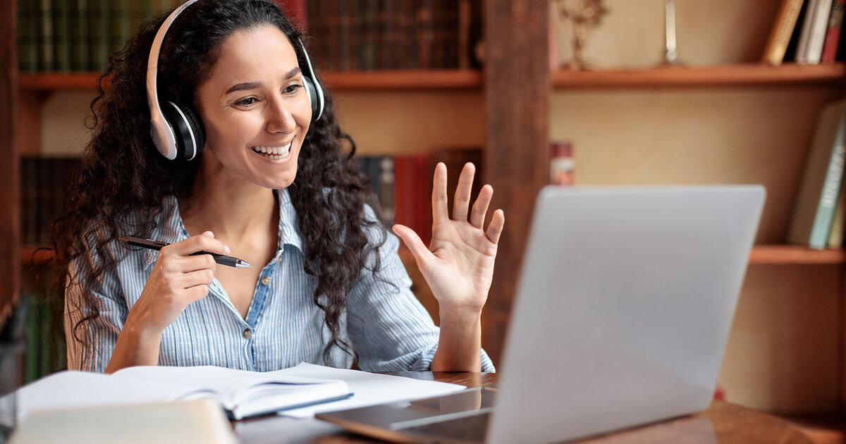 Faculty waving at computer seated at a desk with books