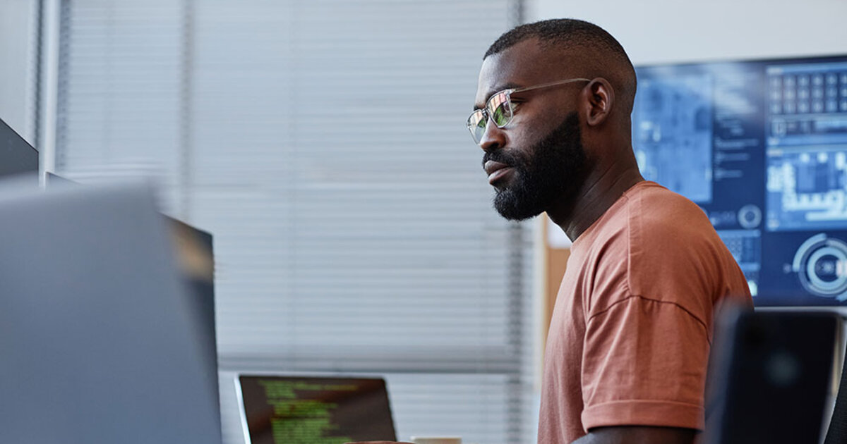 A data professional works at a desk with multiple computer monitors displaying different information.
