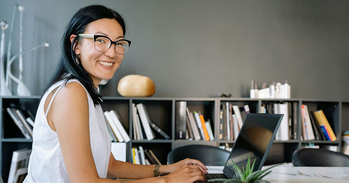 A smiling business women is seated at an office table with a laptop