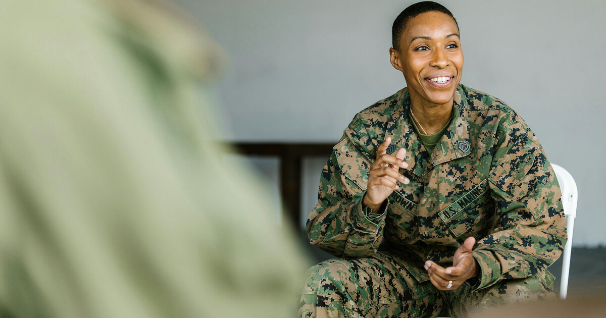 Military member sitting and talking to a group. She is smiling.