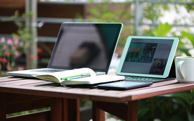 Two open laptops on a wooden desk with a paper notebook nearby