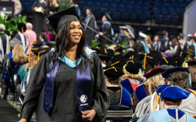 2024 Commencement image of a woman walking to the stage to receive her diploma with a smile