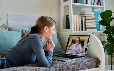 Woman on couch speaking to woman on her laptop