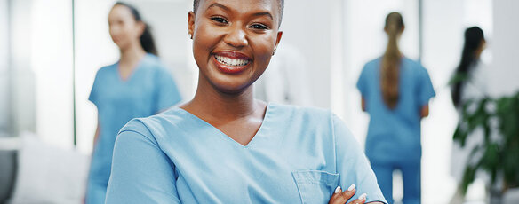 A nurse smiles confidently at the camera in the hallway of a busy medical clinic.