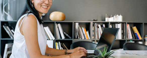 A smiling business women is seated at an office table with a laptop