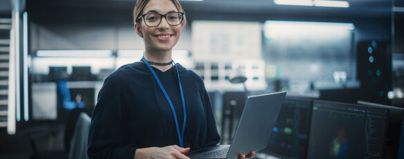 Woman stands holding a laptop in a workspace with servers