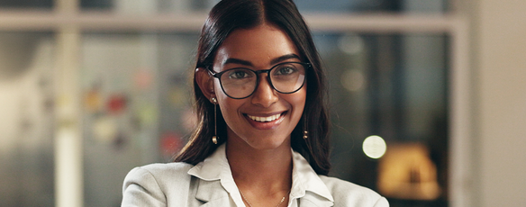 Woman stands smiling in an office with her arms crossed