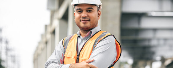 Construction worker stands at a construction site and smiles at the camera, ready to start his journey with ODUGlobal