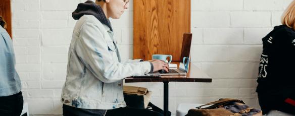 Student sits in a coffee shop on laptop while listening in to a lecture