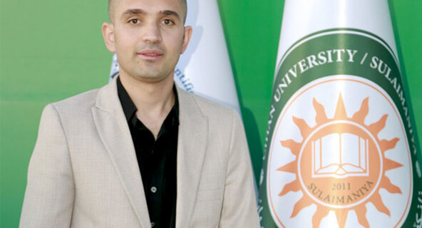 Photo of Sadiq Karim Omer standing next to a flag