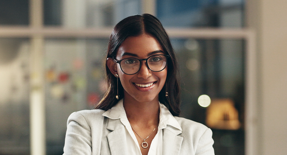Woman stands smiling in an office with her arms crossed