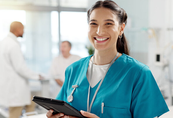 A confiden female nursing gradaute smiles at the camera while holding a tablet device.