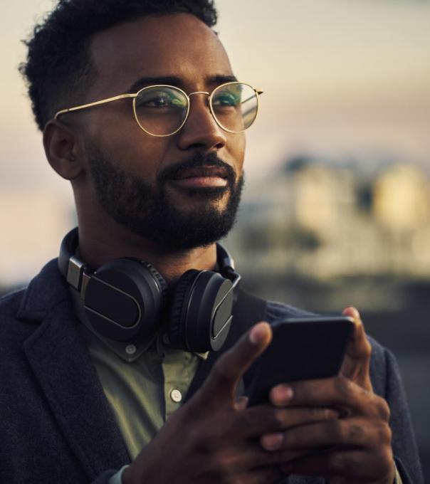 A young African American man holding a mobile phone gazes confidently at the horizon.