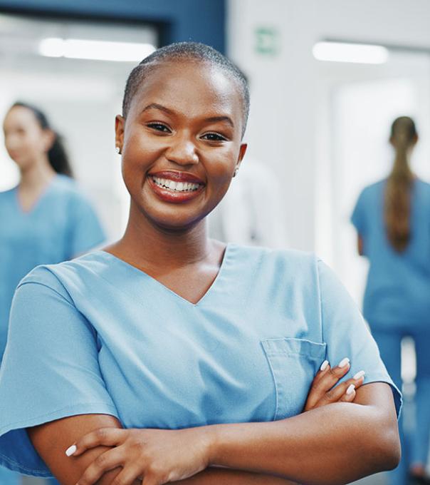 A nurse smiles confidently at the camera in the hallway of a busy medical clinic.