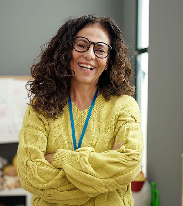 An early education teacher laughs happily in her classroom surrounded by bookshelves and toys.