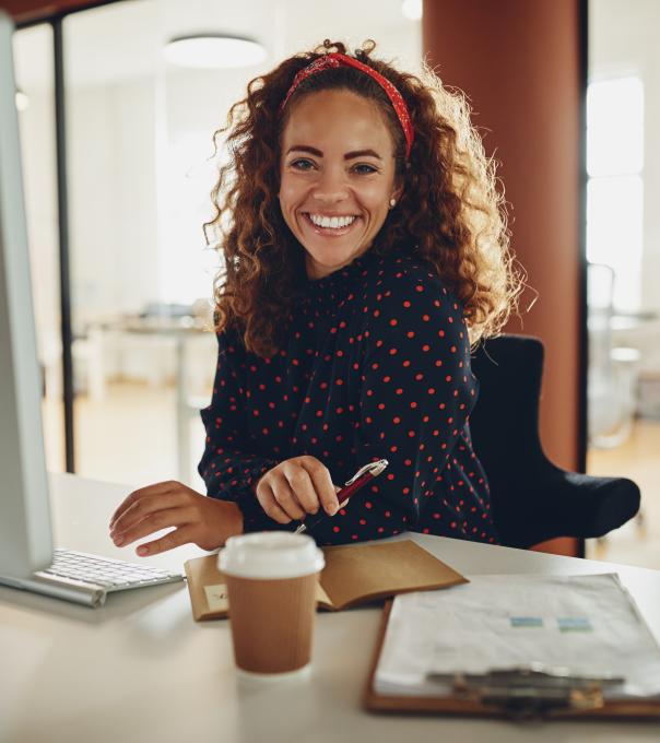 Woman working in accounting smiles at the camera while sitting at a computer. 