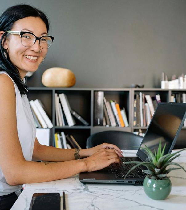 A smiling business women is seated at an office table with a laptop