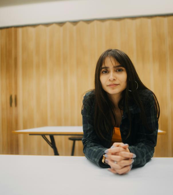 Woman sits at a desk in a classroom and looks at the camera intently 