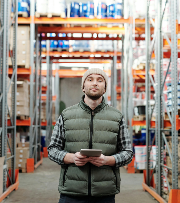 Man stands in a warehouse holding a tablet to direct work.