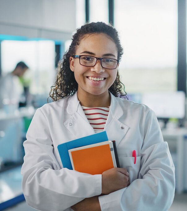 Medical laboratory assistant stands in the lab smiling and holding her books