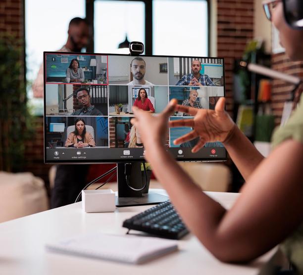 A woman seated at a computer gestures with her hands as she talks to classmates online