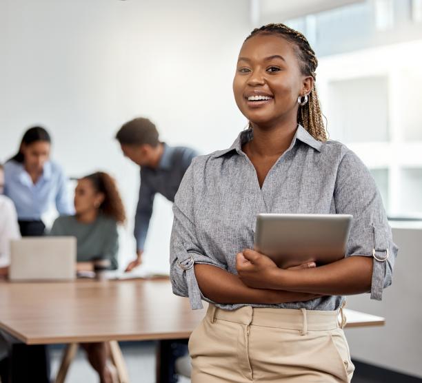 Woman with tablet in a boardroom with colleagues meeting behind her 