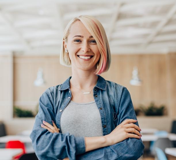 Woman stands in a conference room with arms confidently crossed and smiling.