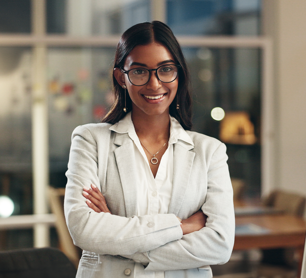 Woman stands smiling in an office with her arms crossed