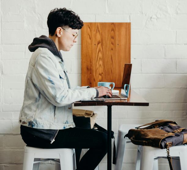 Student sits in a coffee shop on laptop while listening in to a lecture