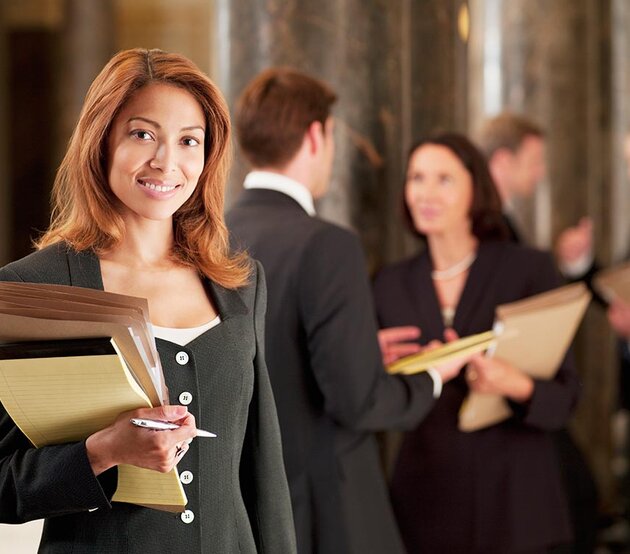 Female professional smiles at the camera while holding a legal pad.