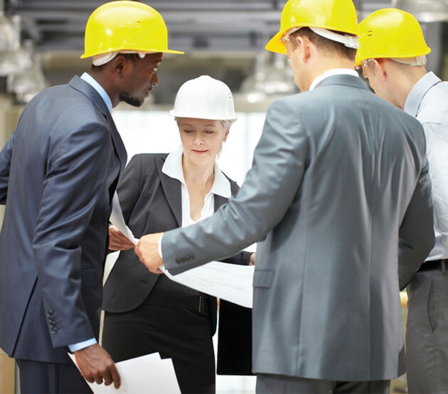 Engineering management staff gather around a large print out in a warehouse setting.