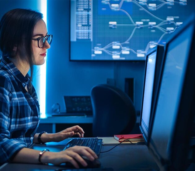 A female professional in the cybersecurity field works at a computer on a desk with dual monitors.