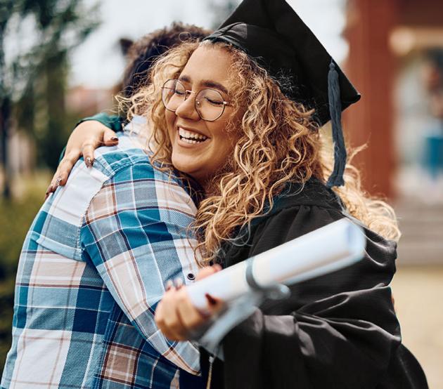 Happy college graduate hugs a family member outside on a sunny day.