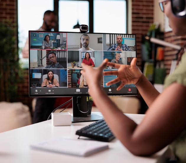 A woman seated at a computer gestures with her hands as she talks to classmates online