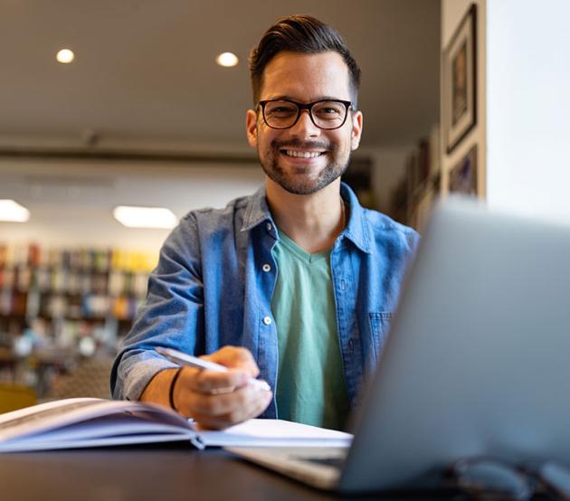 Student at desk with computer and books, smiling at the camera.