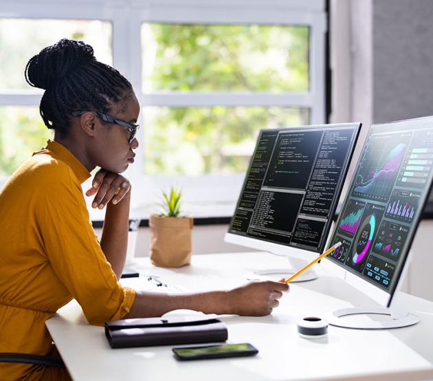 A data science professional reviews code and data visualization charts on a desktop computer. Explore degrees in Data Sciences today!