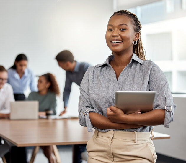 Woman with tablet in a boardroom with colleagues meeting behind her 