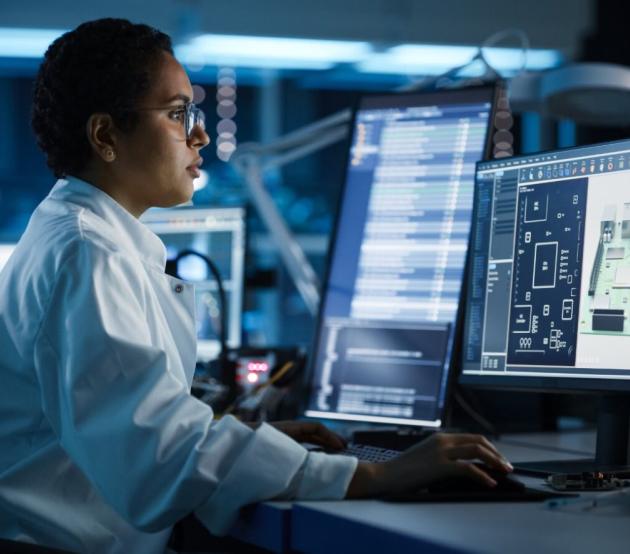 Woman at a computer desk with several screens looks at technical information