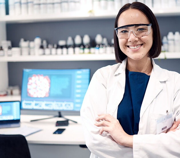 A clinical laboratory specialist stands confidently in front of a computer for health research.