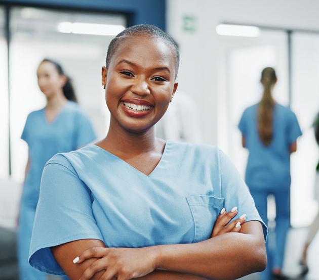 A nurse smiles confidently at the camera in the hallway of a busy medical clinic.