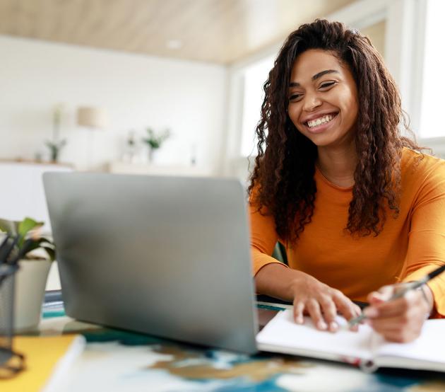 Woman in gold sweater sits at a desk and smiles at her computer while writing