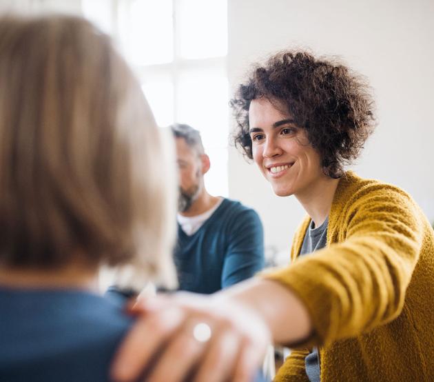 Woman sits with a group and extends hand to place it on the shoulder of another woman.