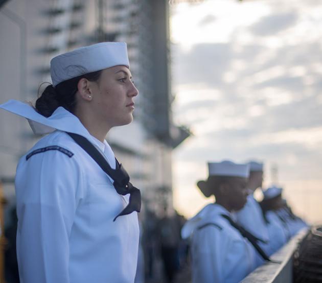 Enlisted Navy personnel stand at attention on the deck of a ship at sea.