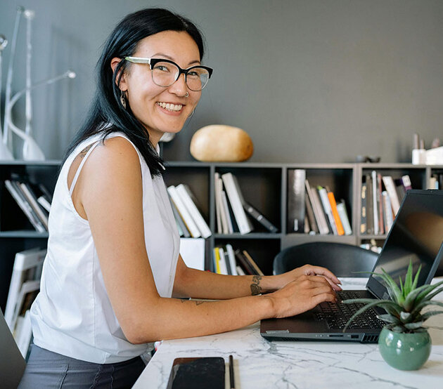 A smiling business women is seated at an office table with a laptop