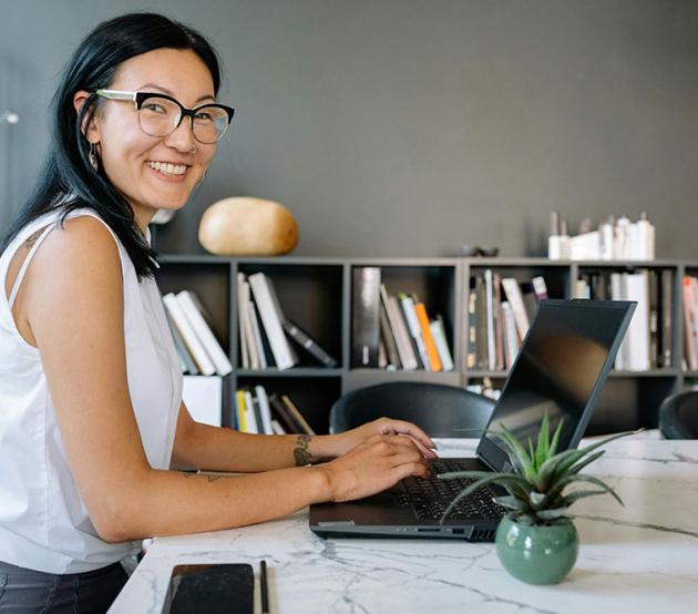 A smiling business women is seated at an office table with a laptop