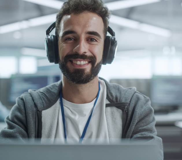 Student sits at his computer in a shared office space smiling at the camera