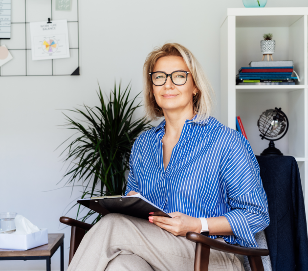 A counselor sits holding clipboard and smiling at the camera
